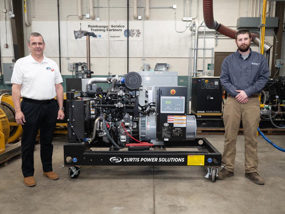 Two people stand next to a gaseous-fueled generator set