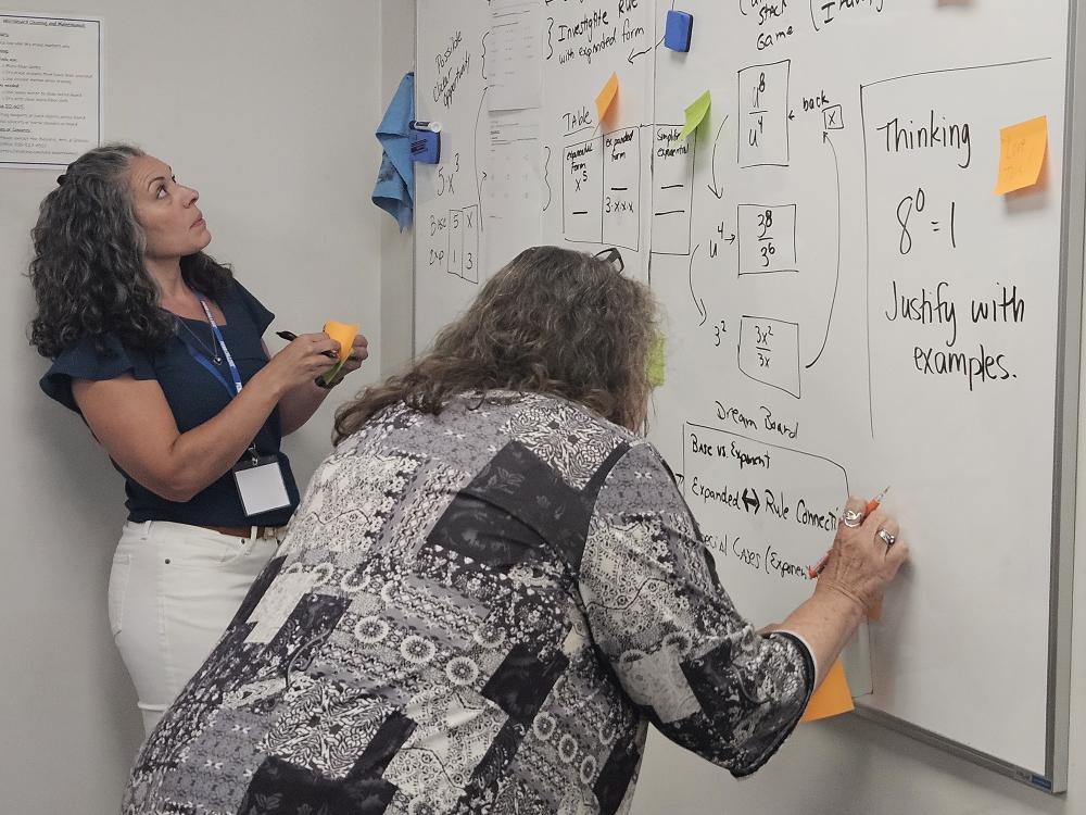 Two people write on a whiteboard