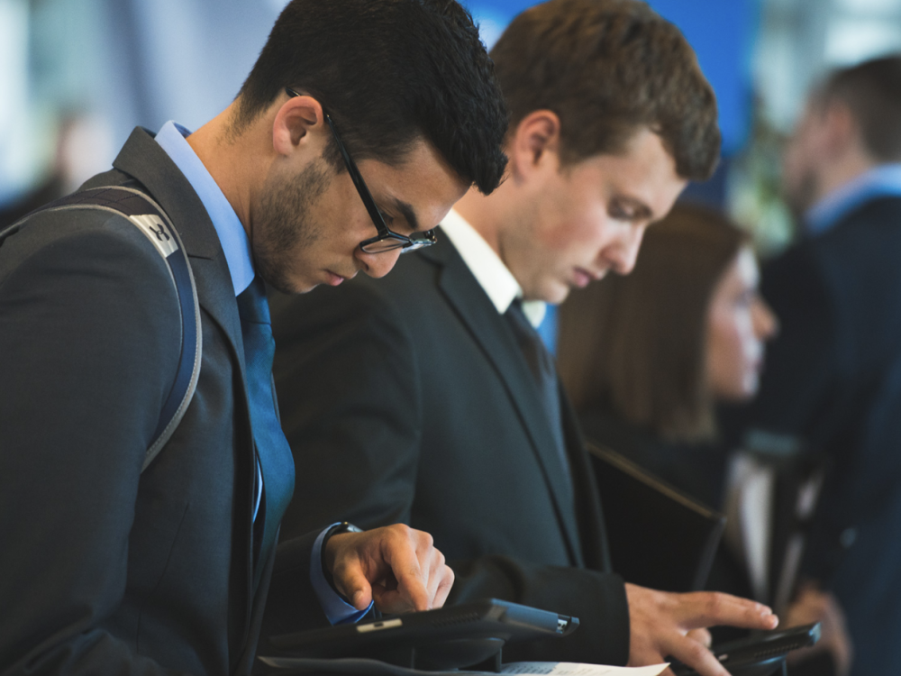 Students in business attire looking down at tech device