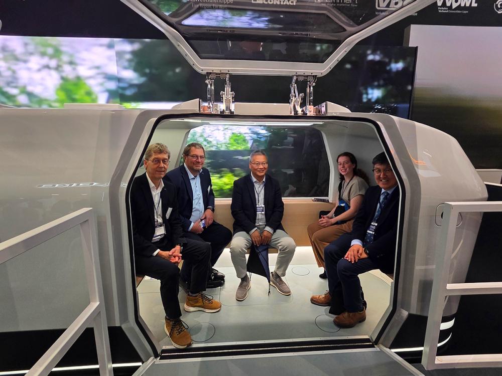 Five adults sit together and smile inside a modern vehicle cabin.