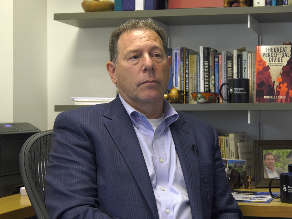 Mitchell Smith seated in front of a bookcase with his book "The Great Perceptual Divide" on the shelf facing the camera