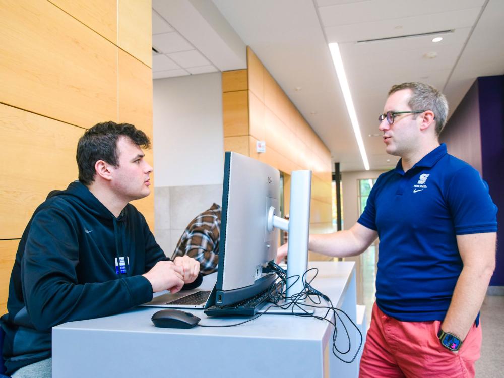 Two men talking near a computer