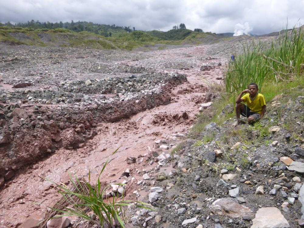A child sits next to a stream with reddish water. Penn State researchers are studying the area near a gold mine in Papua New Guinea. 