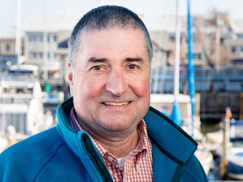 Penn State chemical engineering alumnus and Chesapeake Bay Program Director Dana Aunkst in blue fleece with a Chesapeake Bay boat dock behind him. 