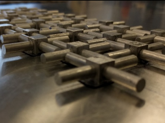 Several metal structures, each with four horizontal arms, lie horizontally on a sheet of aluminum.