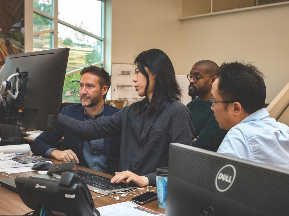 Four people sit around a monitor in a design office