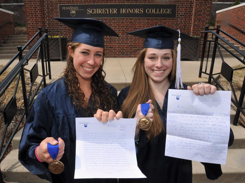 Schreyer Scholars Jessica Paholsky, left, and Cori Steimling pose in cap and gown with Schreyer Scholars medals and letters they wrote to themselves in August 2010.