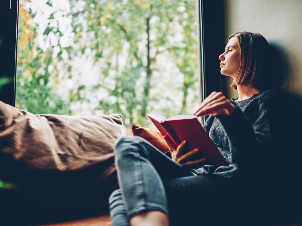 A woman reading a book on a window bench