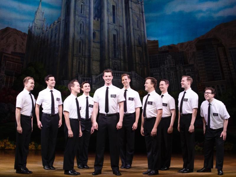 A group of men wearing matching button-down shirts and slacks smile while they stand in a row.