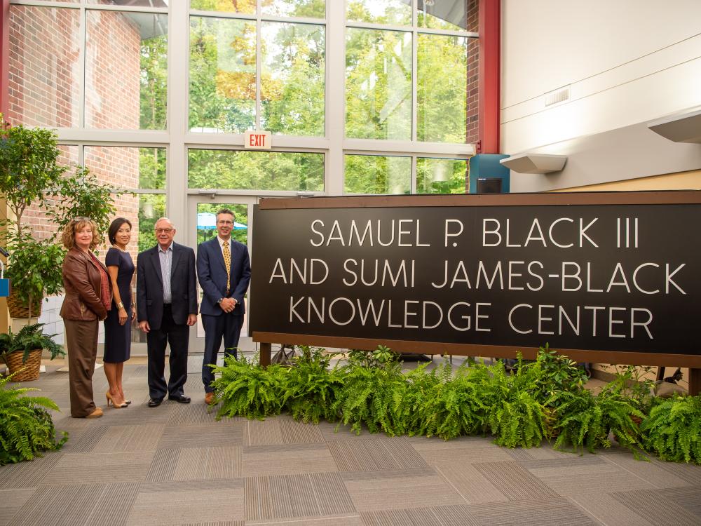 Four officials stand near the new sign for the Samuel P. Black III and Sumi James-Black Knowledge Center