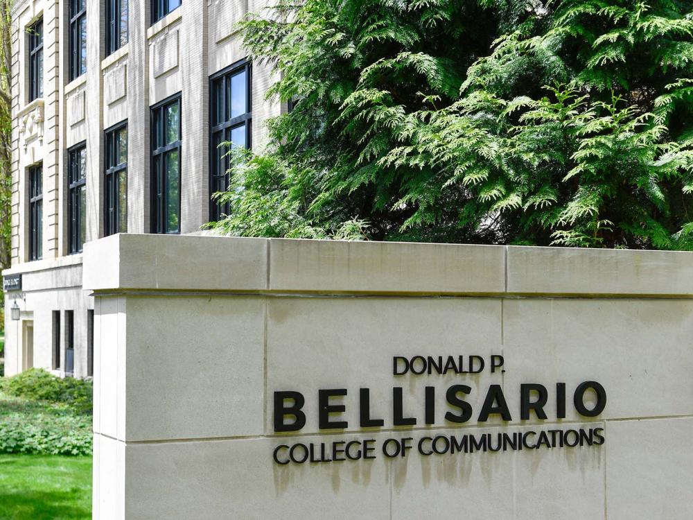 The name "Donald P. Bellisario College of Communications" is shown on a stone wall in front of the Carnegie Building at Penn State.