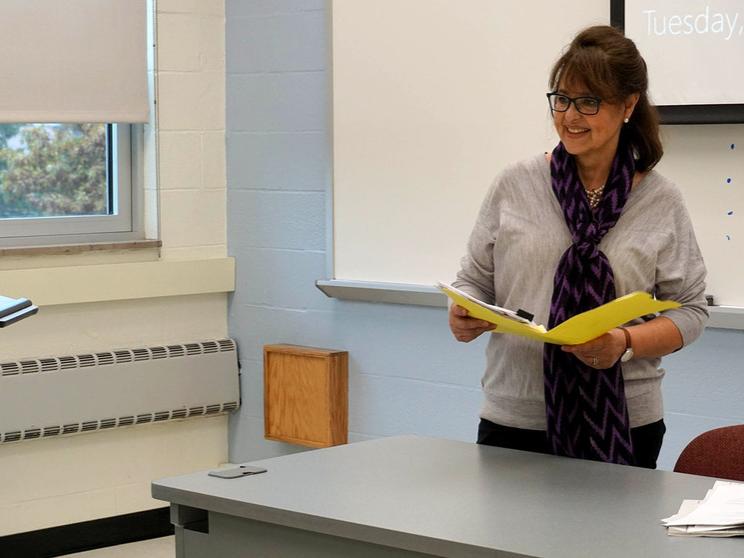 Woman smiling holding book behind a desk. 