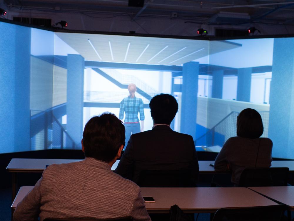 men and women sitting in front of a large virtual reality screenFujita visitors reviewing virtual building model in Immersive Construction Lab