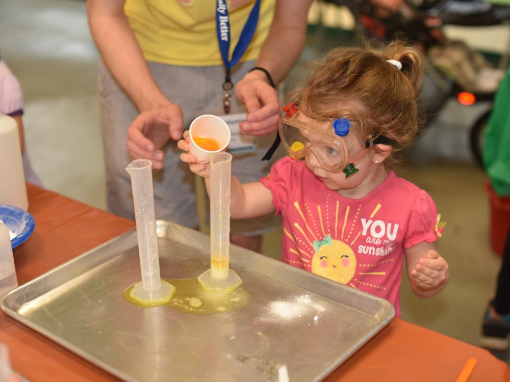 Young preschool-aged girl pours fluid into a beaker.