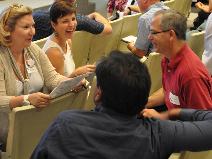 Faculty members sit in small groups discussing and laughing