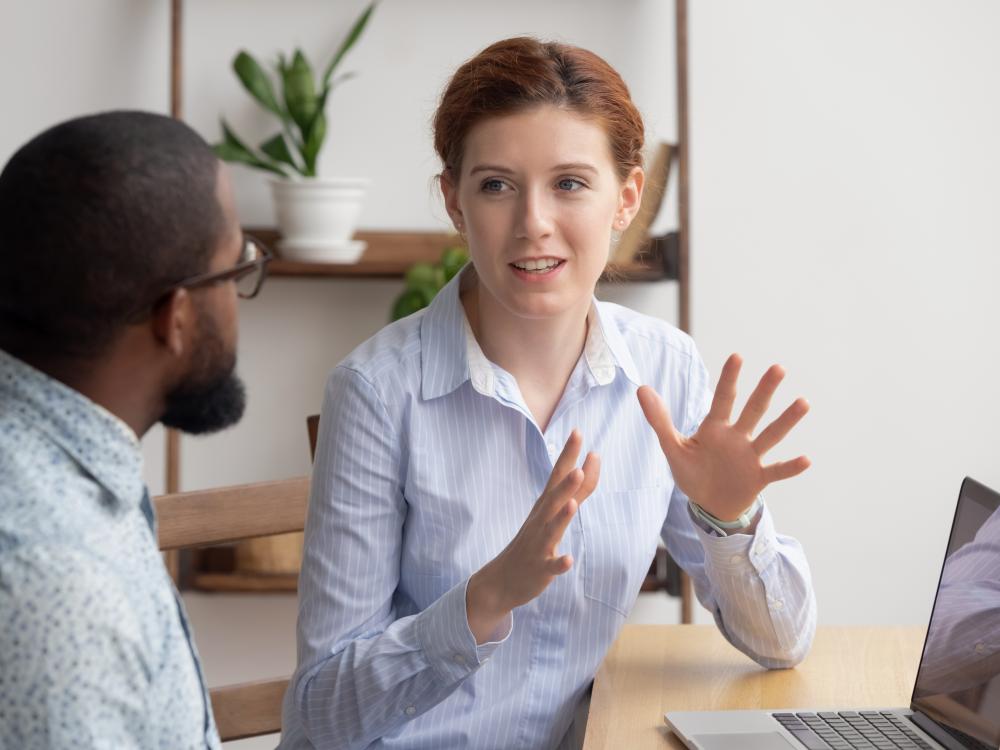 Man and woman talking near a laptop computer in an office setting. 