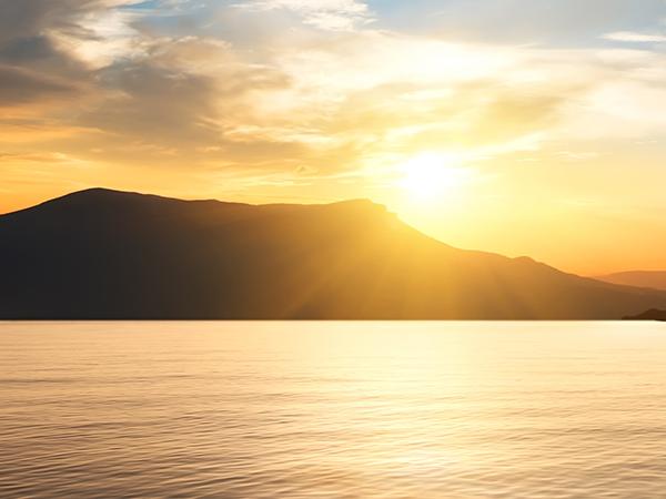 The sun setting behind a mountain overlooking calm waters