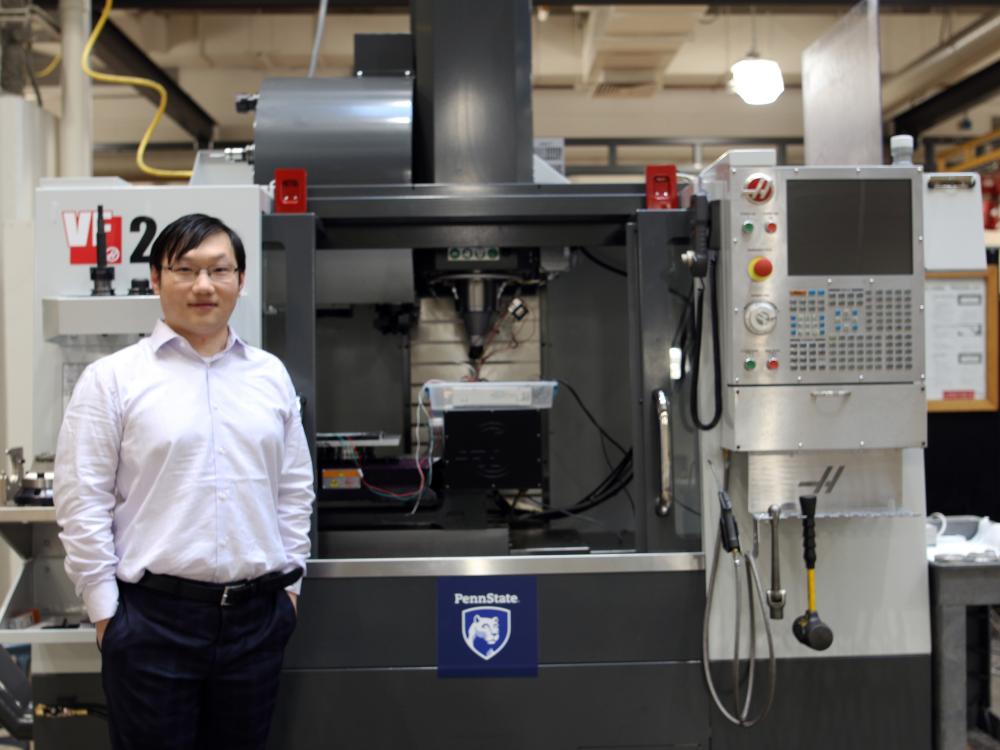 A man standing in a lab in front of a machine on the floor.