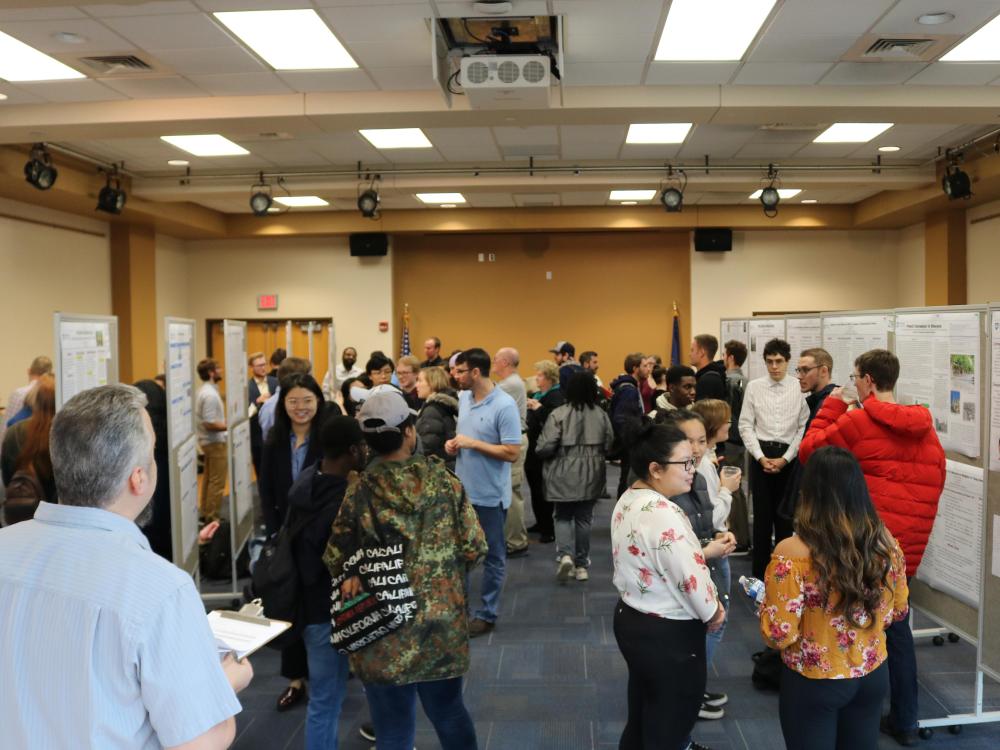 a big room with research poster on pin boards and a lot of people reviewing the research.