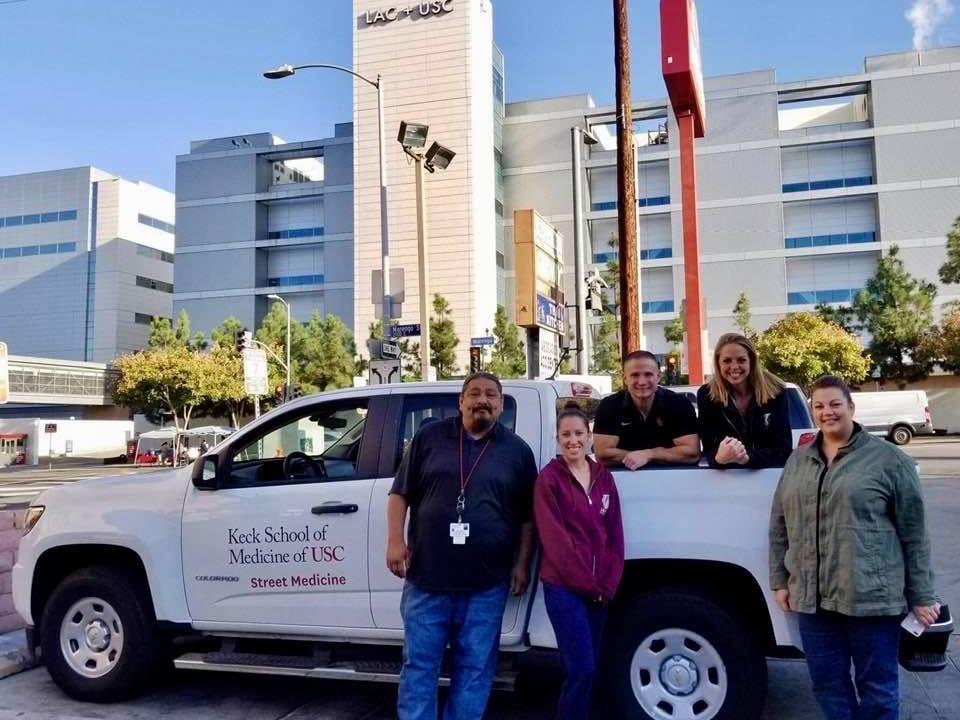 Brett Feldman and some of his team members stand by a white pickup truck in front of a hospital in LA