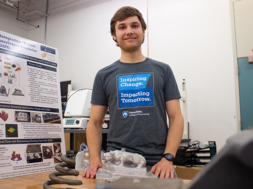 A man stands in an additive manufacturing lab with posters and equipment.