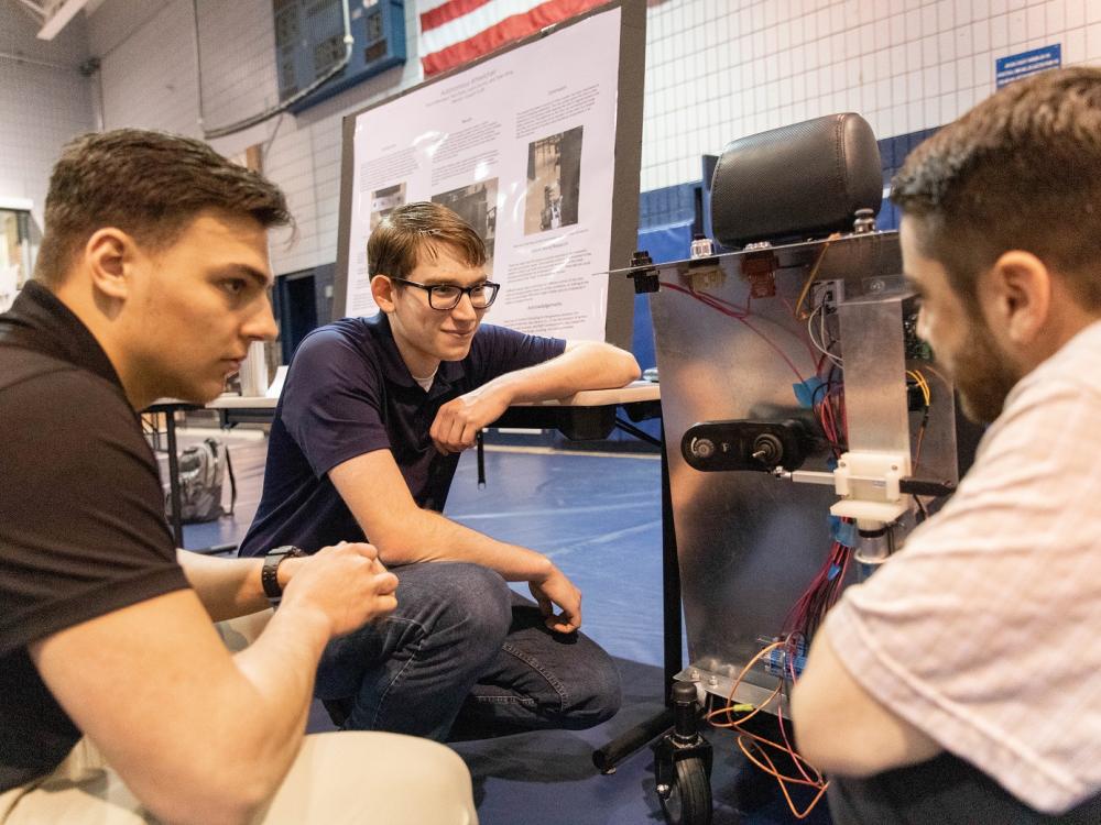 Three male students look at autonomous wheelchair