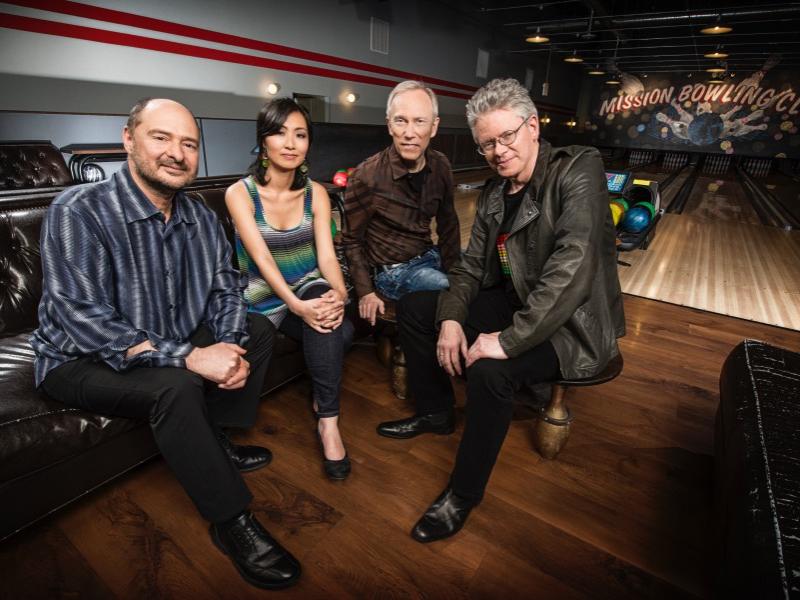 Four people sit in a bowling alley and smile for the camera.