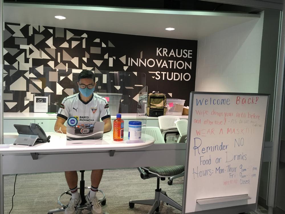 A masked student sits at a reception desk at the entrance to the Krause Innovation Studio