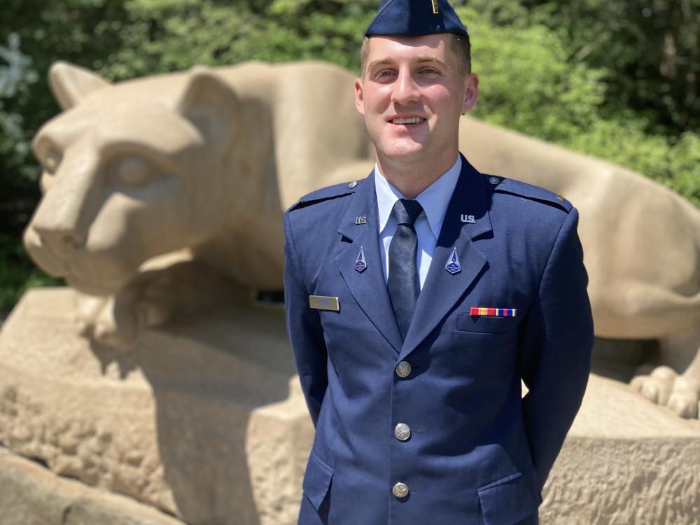 person dressed in air force uniform stands at ease in front of lion status for picture.