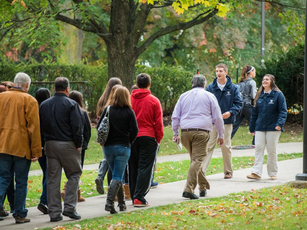 Two students walk backwards to lead a campus tour group.