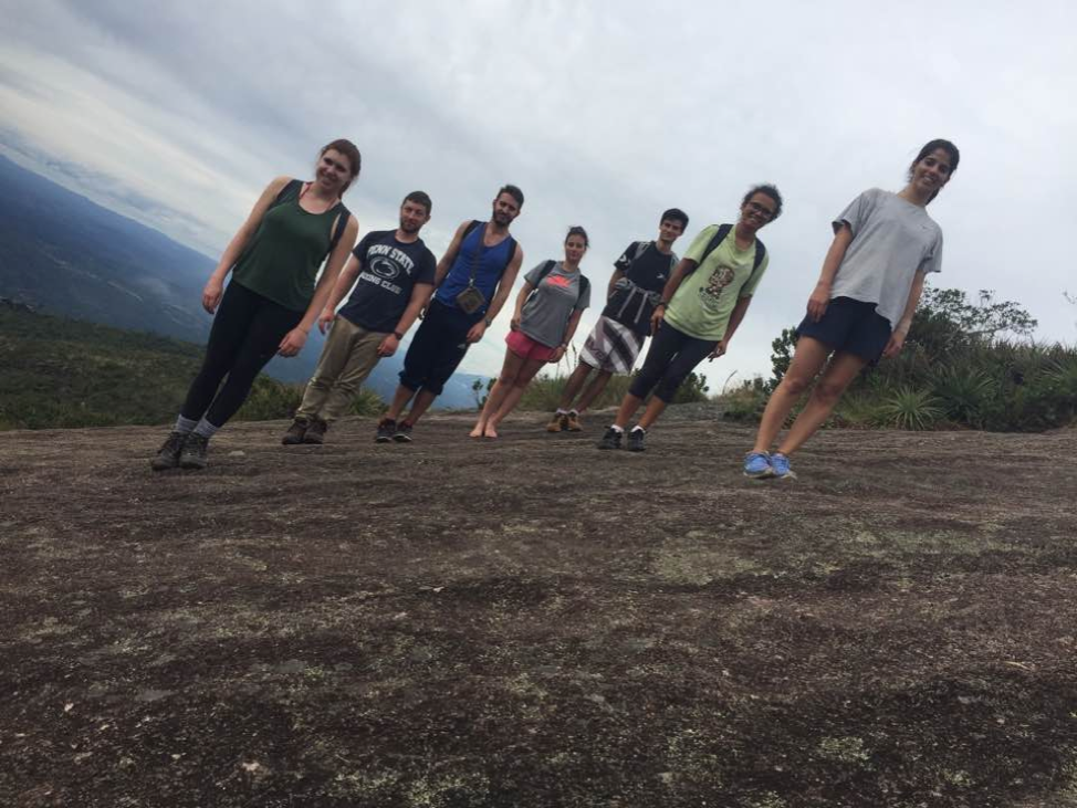 A group of hikers pose on a hill, looking as though they are all leaning to the right