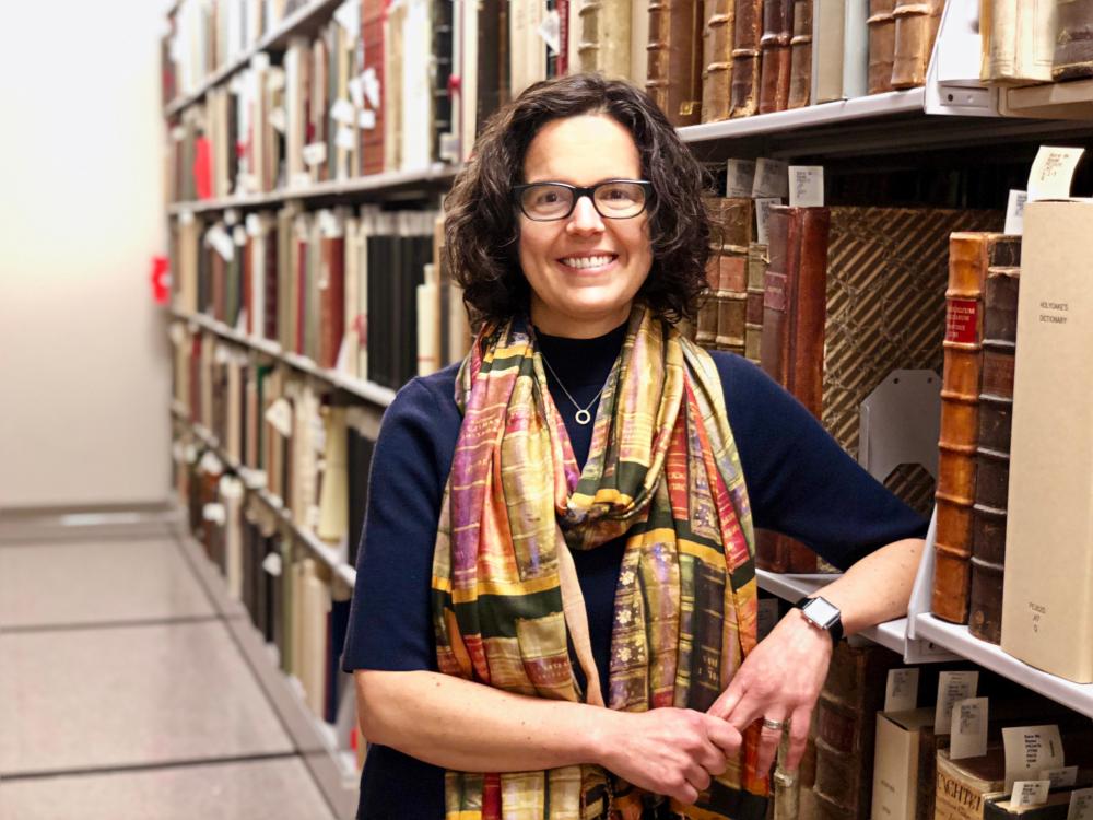 woman standing next to shelves of old books