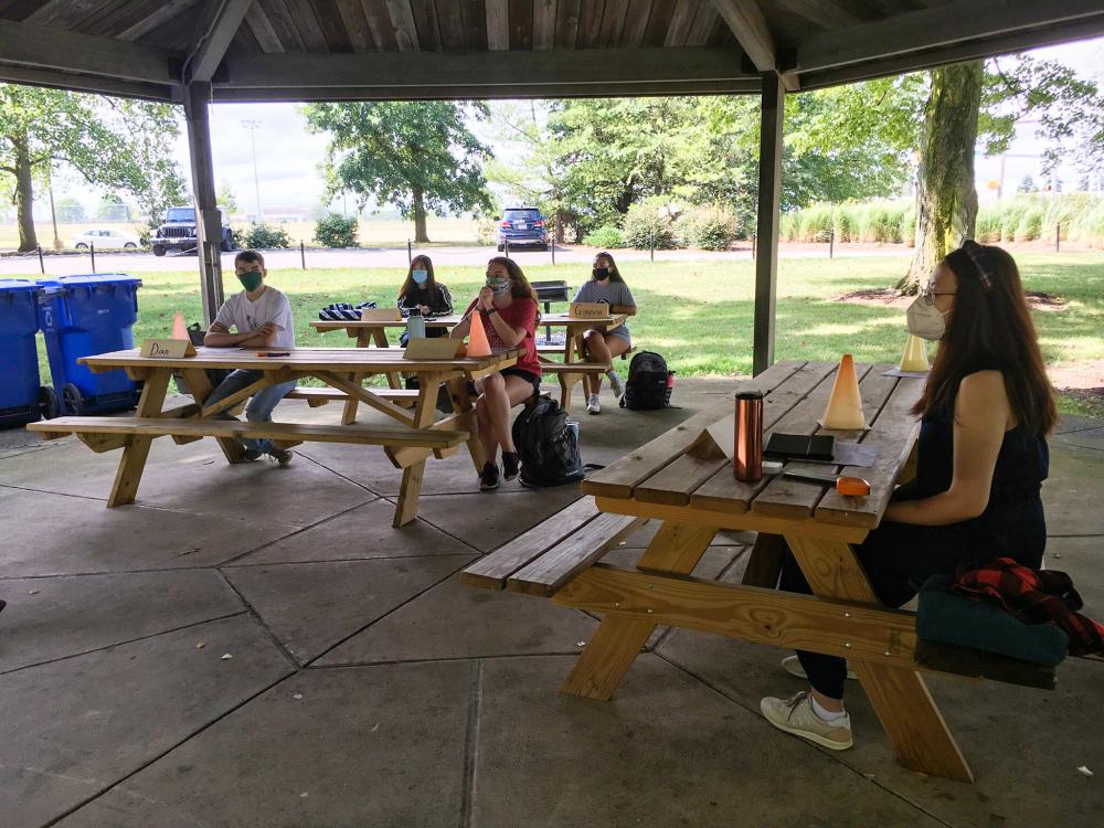 Students sitting socially distanced at picnic tables for an outdoor class.