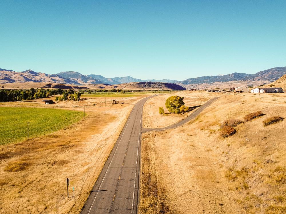 Lonely road seen from above through dry Montana countryside with one house in the background