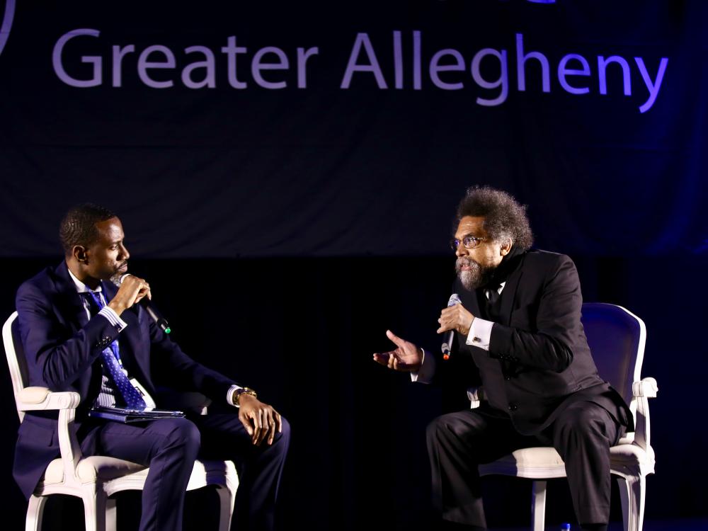 two men sitting on stage talking into microphone