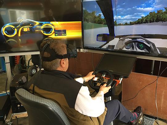 Man sitting in front of large TV screens driving an augmented reality vehicle