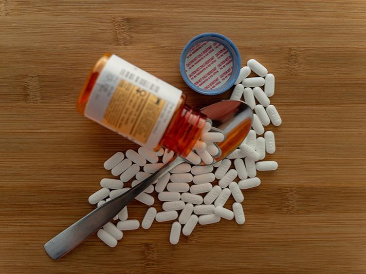 Prescription pills spilled out of the bottle onto a wooden table with a spoon