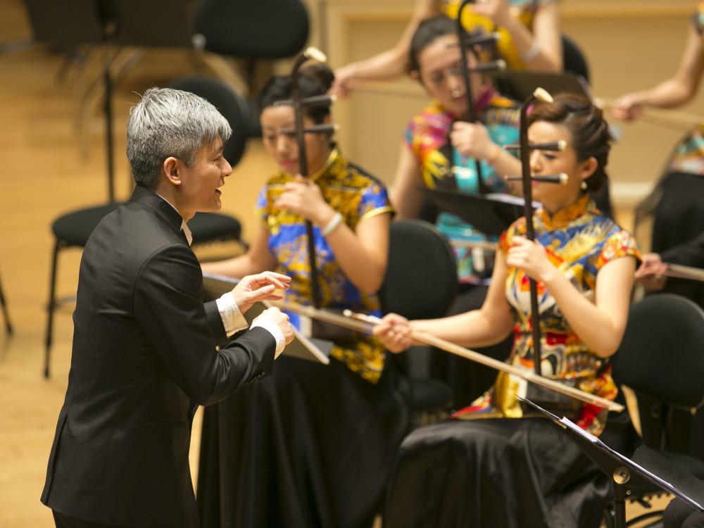 A conductor leads musicians who are playing traditional Chinese instruments.