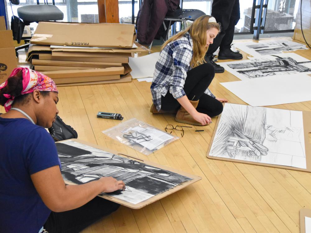 Two students sit on the floor drawing with charcoal at the Robert Reed Drawing Workshops at Penn State.