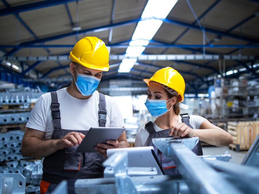 Two masked manufacturing workers in a manufacturing/factory setting