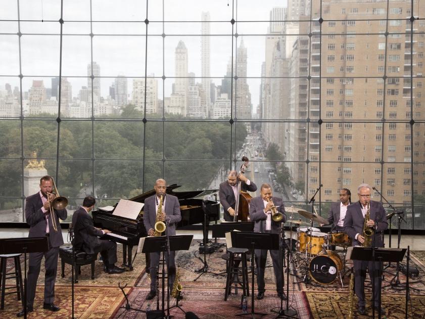 Jazz musicians perform at Lincoln Center in front of window with New York City as backdrop.