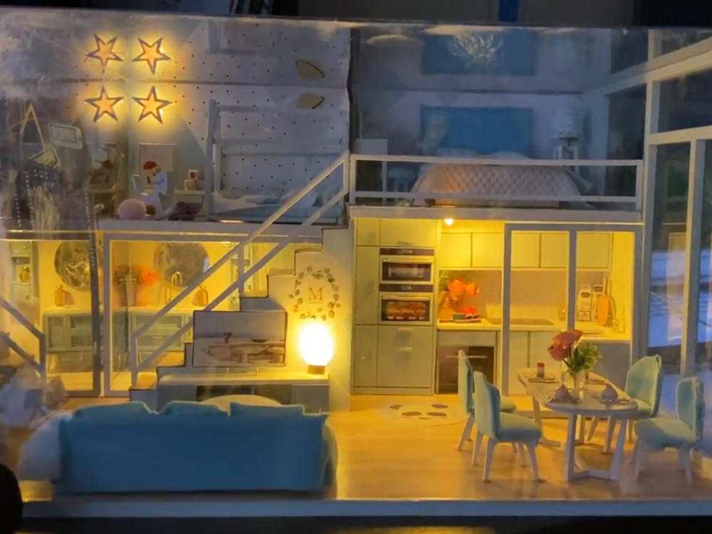 A small-scale house that fits on a table top and is outfitted with lights and small pieces of furniture, simulating a life-size smart house.