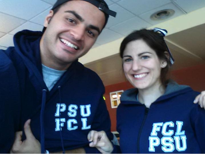 Graduate student and professor smile and pose wearing blue sweatshirts