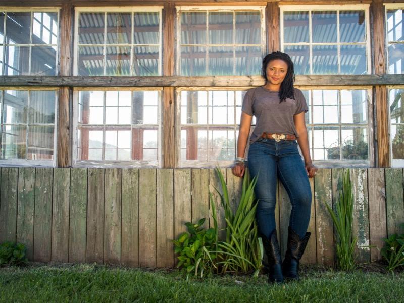 A woman leans against a row of windows and smiles.