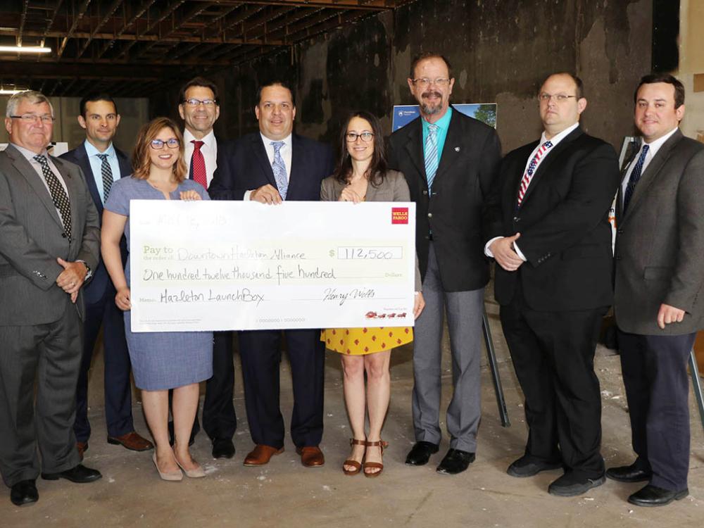 Nine smiling people standing with large check.