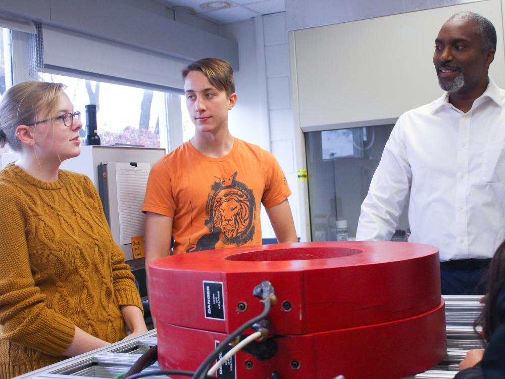 Two graduate students and a professor stand near a magnetic separation device, discussing their research.