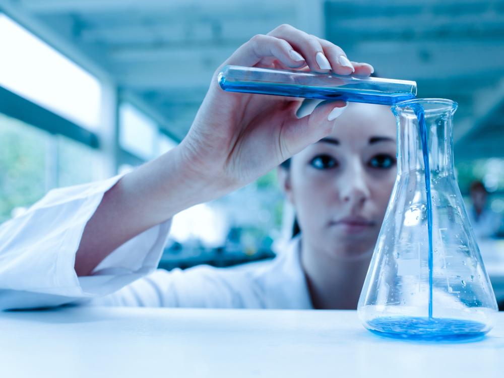 A laboratory researcher pours blue liquid in a container.