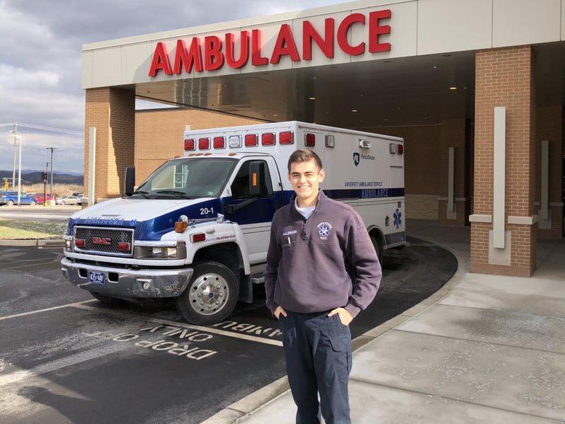 Man in blue pullover stands in front of an ambulance outside a hospital.