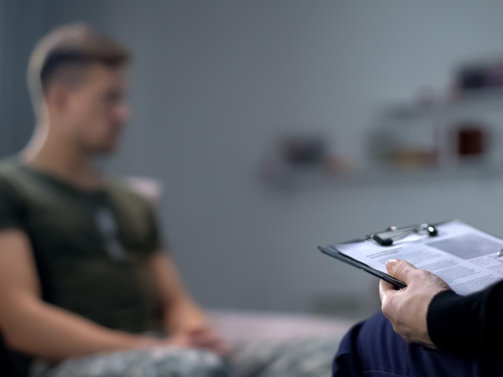 Psychologist making notes during therapy session with sad male soldier