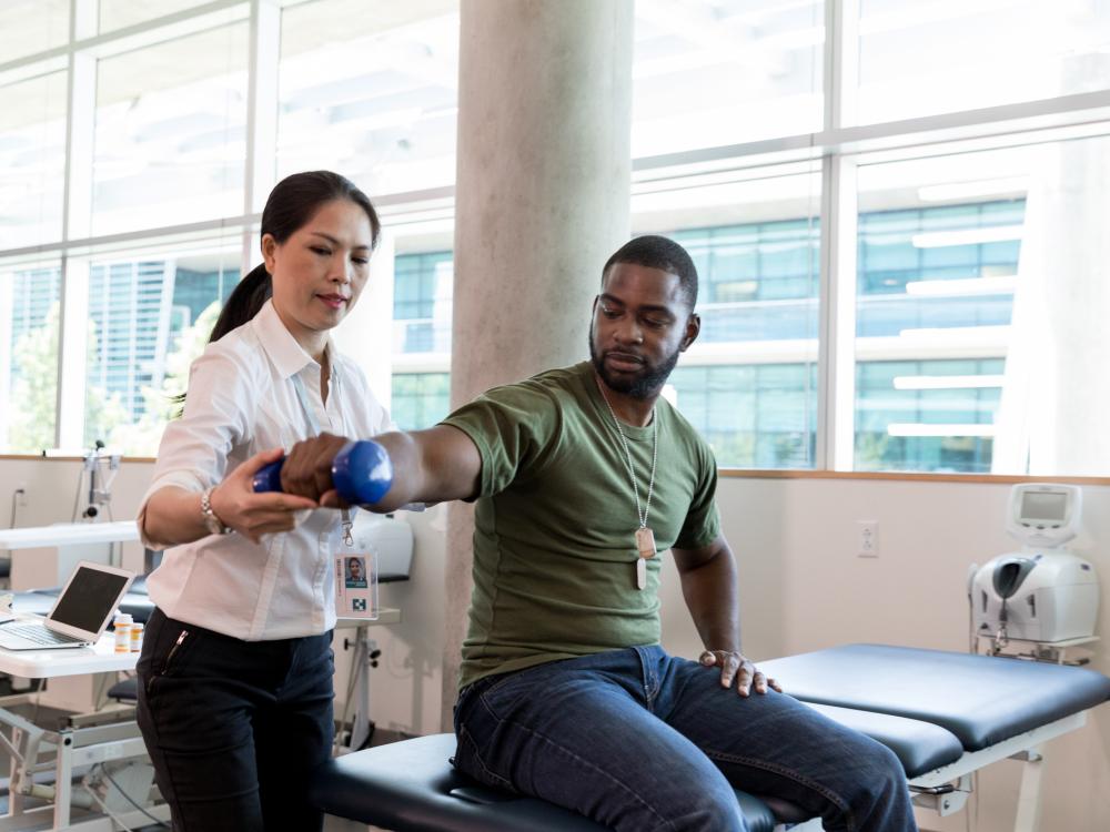 A female doctor helps a male veteran patient with physical therapy on his arm.